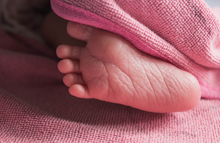 Little right foot of newborn baby under pink blanket