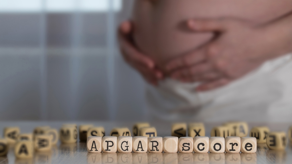 Words APGAR SCORE composed of wooden letters and pregnant woman in the background