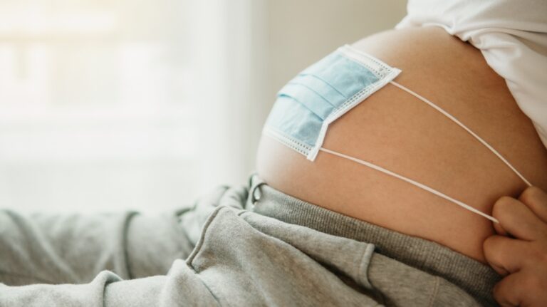 A pregnant woman covers her belly with a mask to protect against viruses